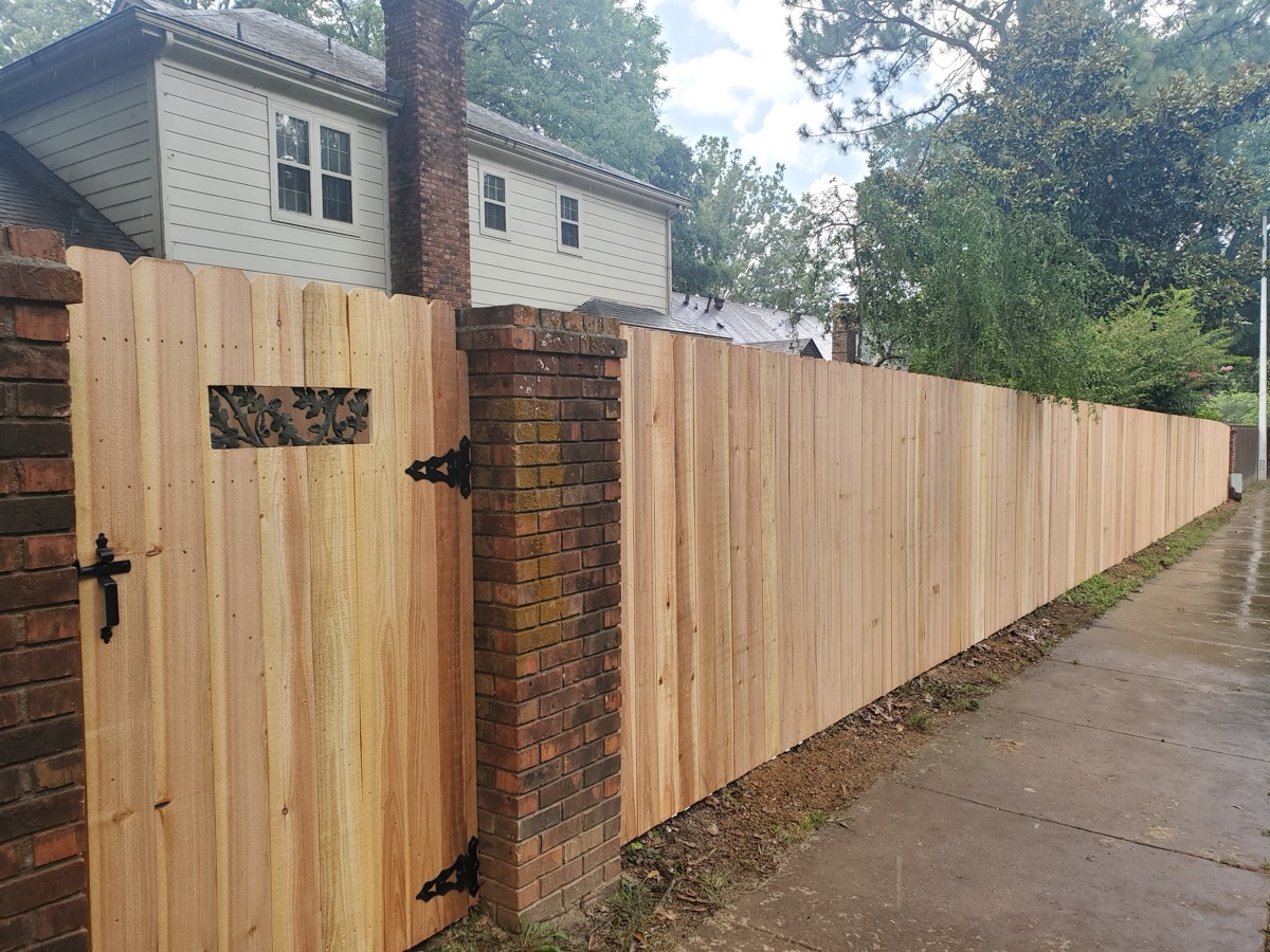 Cedar gate with brick columns and decorative iron hardware along fence line