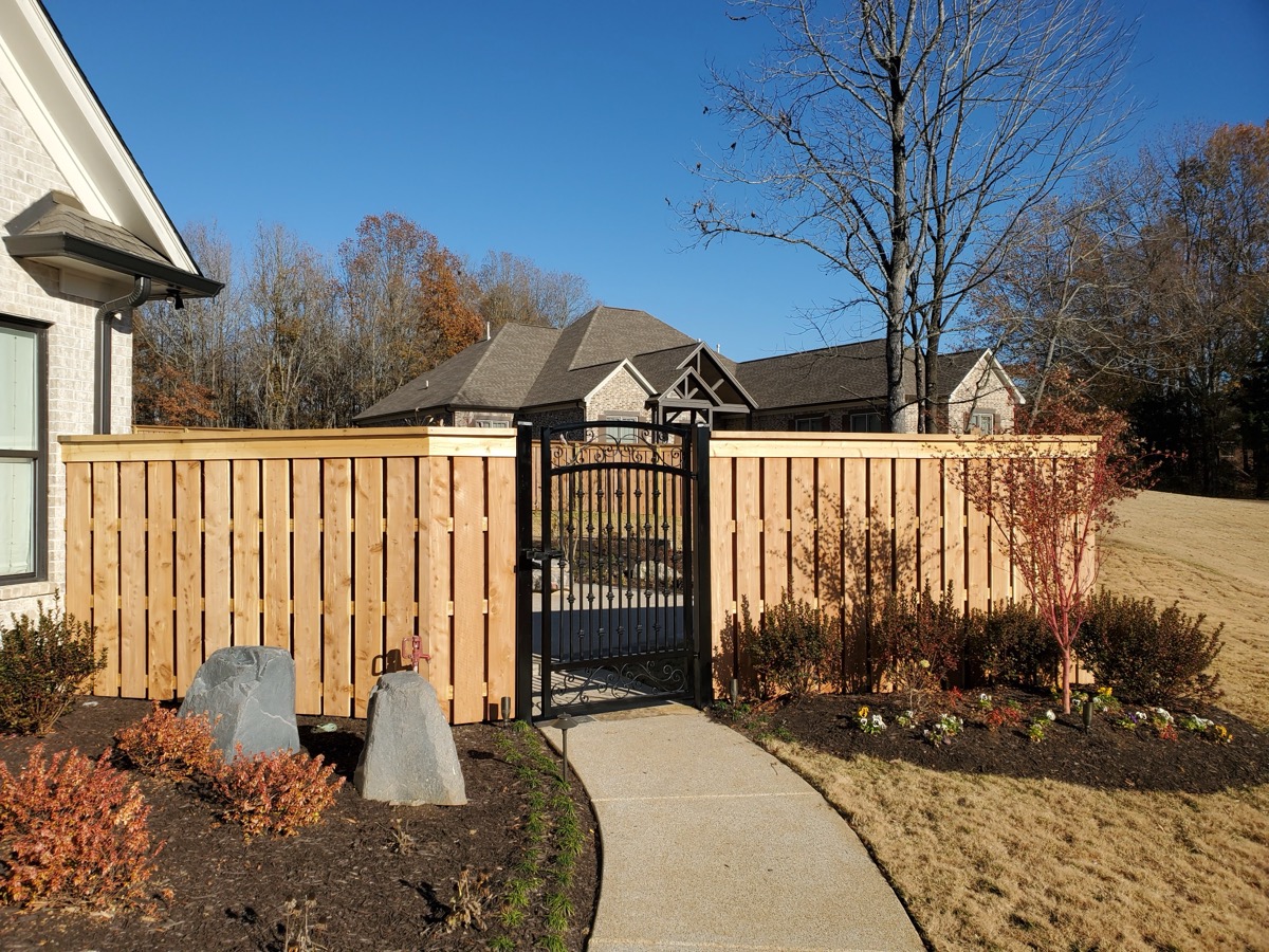 Shadowbox fence with decorative iron gate and walkway landscaping