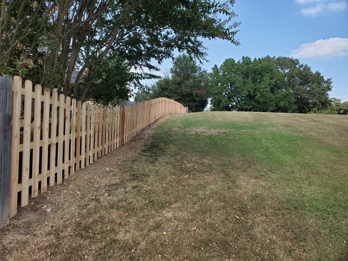 Picket fence running along open field with mature trees