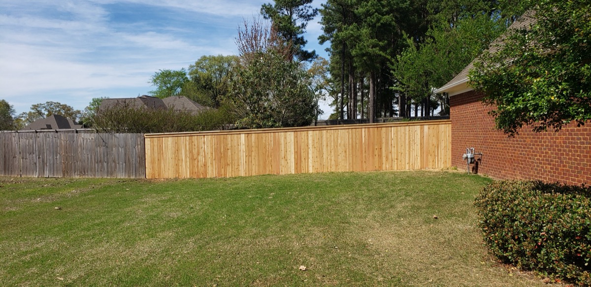 Privacy fence along brick house with manicured lawn