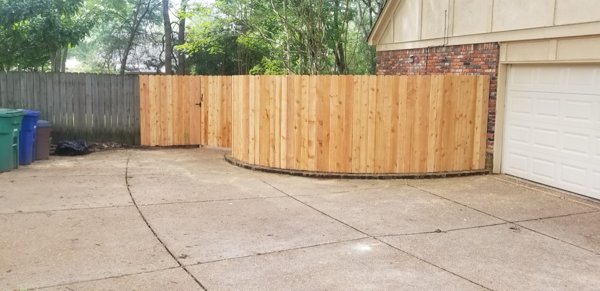Privacy fence curving along driveway beside garage